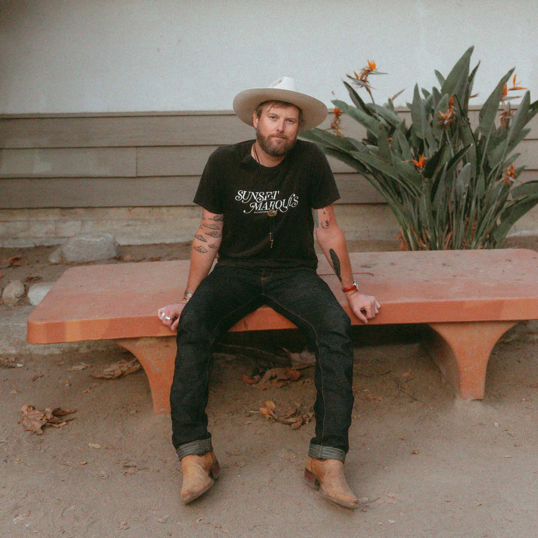 Drew Kennedy wearing a wide-brimmed hat in front of succulent plants